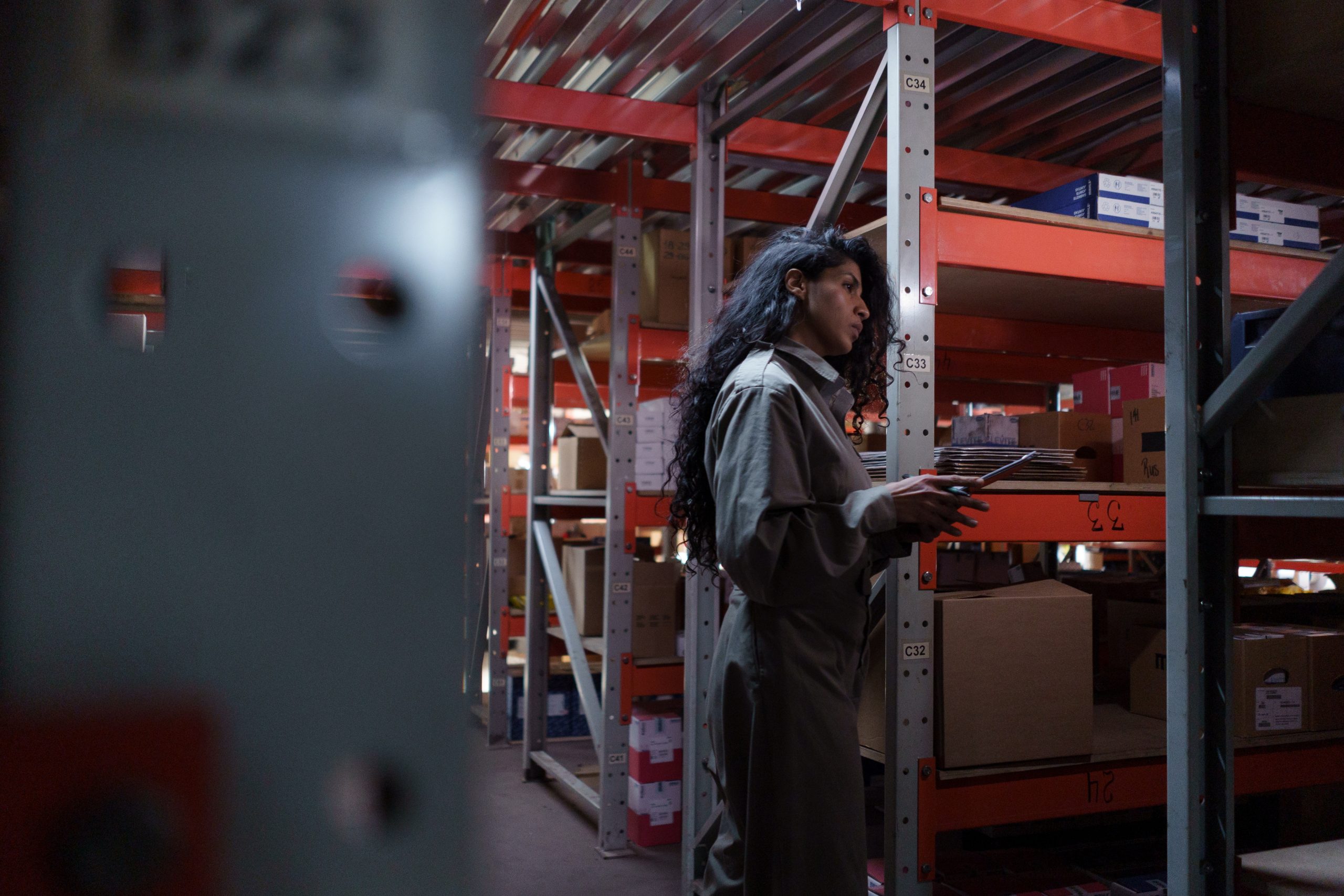 woman with long, curly dark hair with tablet working in warehouse